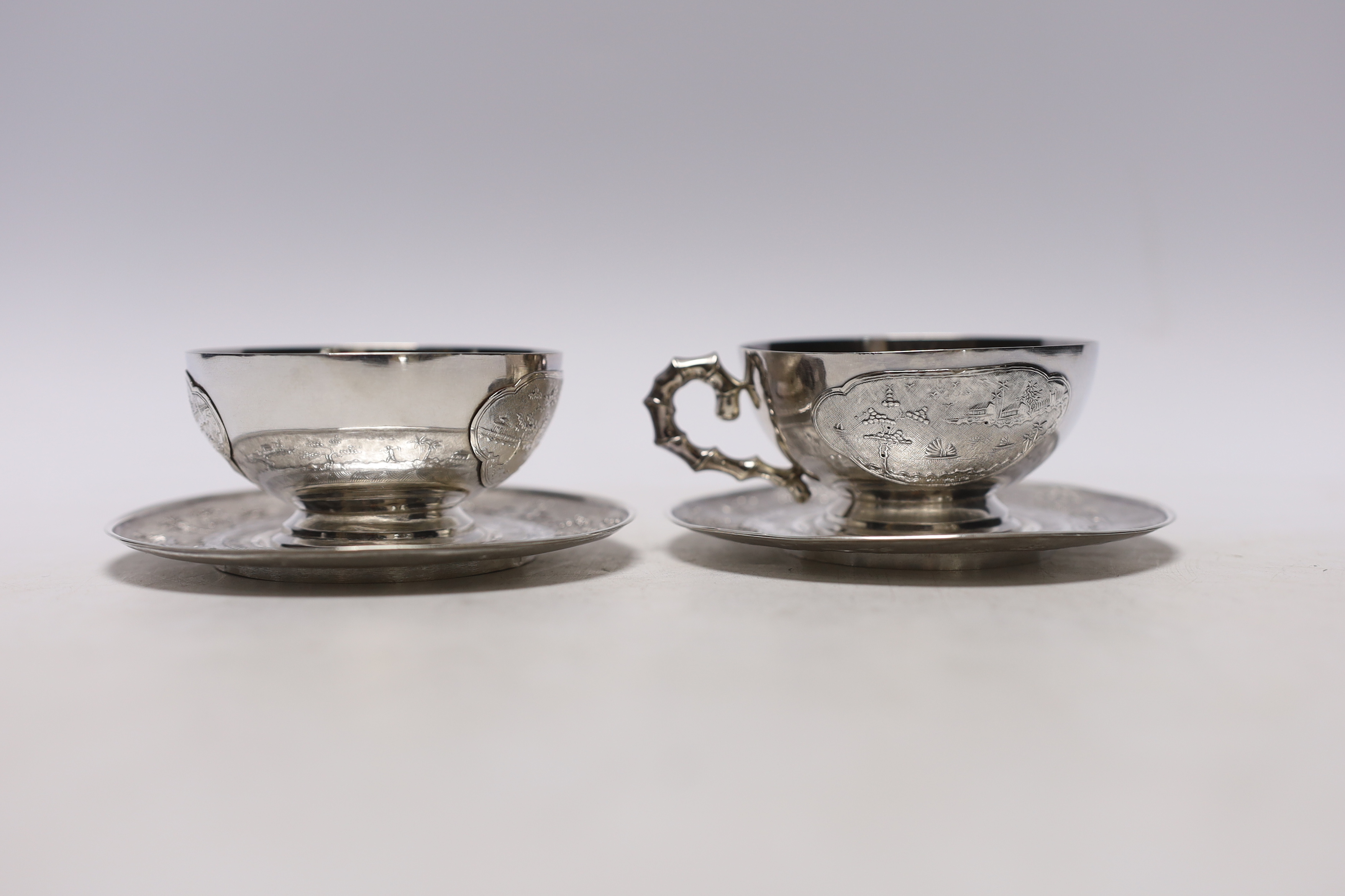 Two early 20th century Vietnamese 800 standard white metal tea cups and saucers (one lacking handle), saucer diameter 10.1cm, 6.6oz.